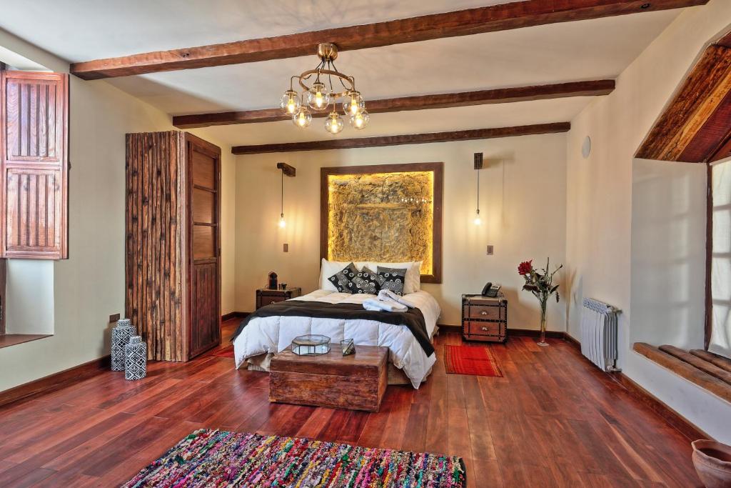Rustic bedroom with dark wood floors, exposed ceiling beams, a centered bed under a large gold-framed artwork and pendant lights on each side.