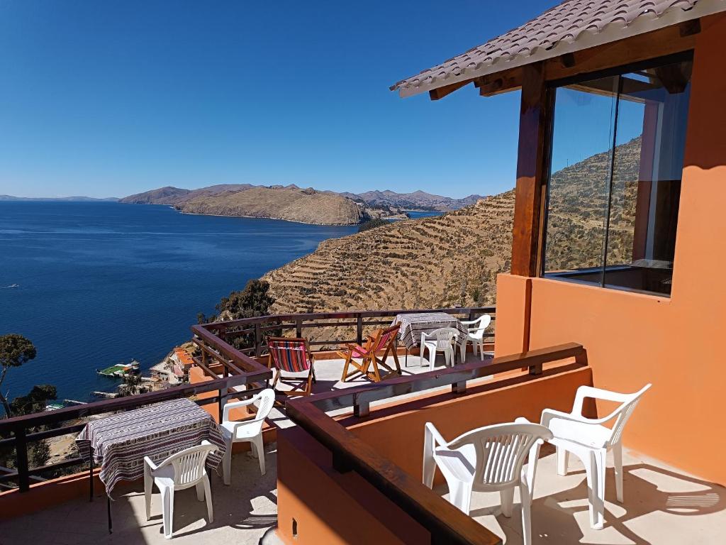 Terrace with orange walls and white plastic chairs, overlooking blue sea and terraced hills.