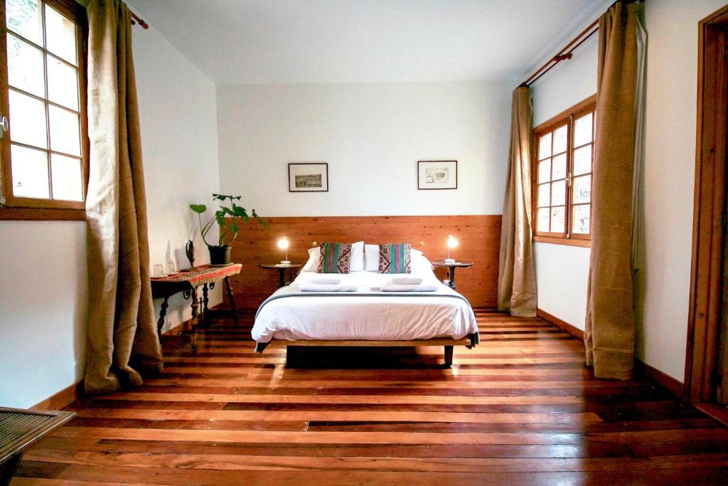 A cozy bedroom with a low bed, white bedding, and colorful throw pillows, flanked by two small nightstands and lamps.