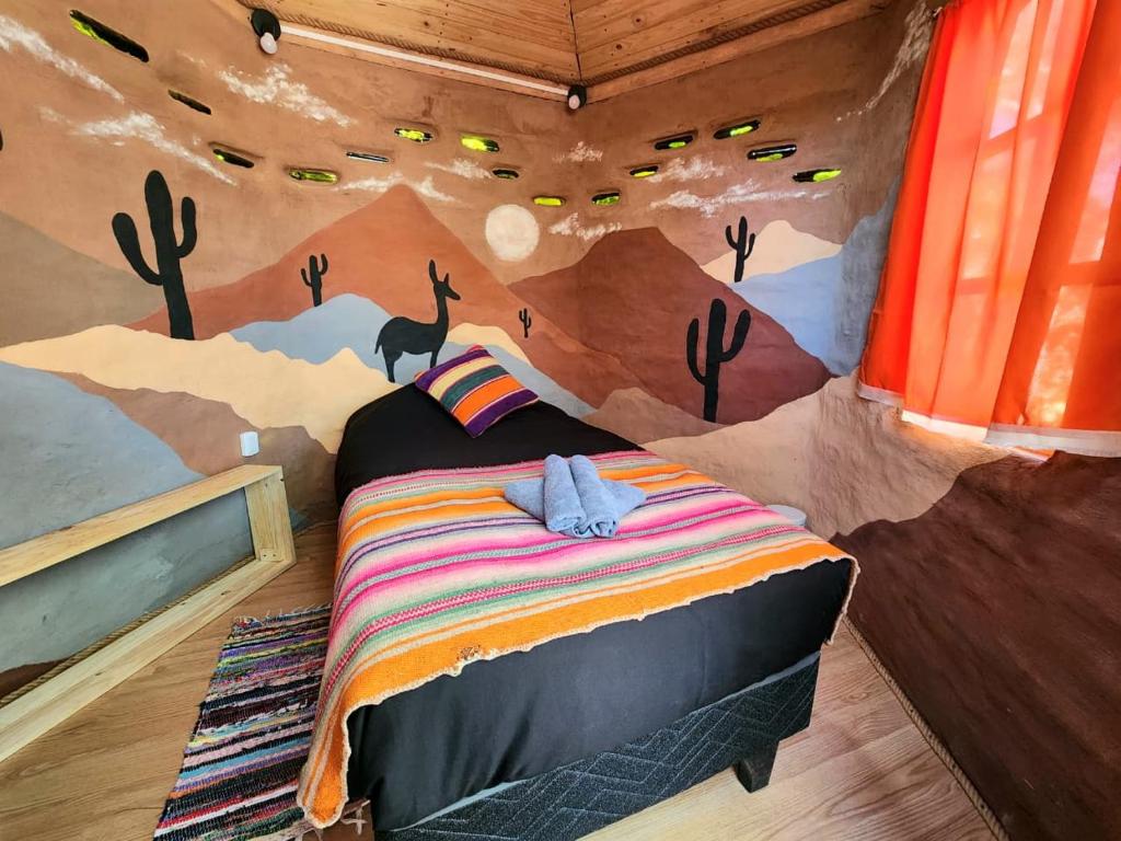 Small bedroom with desert mural walls featuring cacti and mountains, a bed with an orange striped blanket and a towel on top.