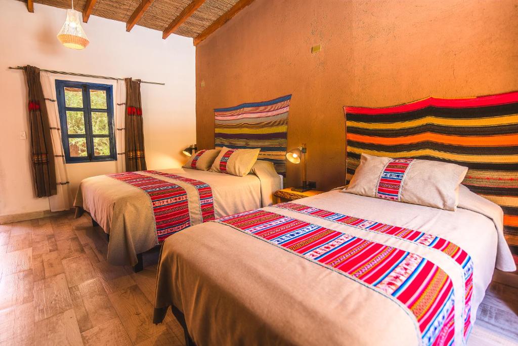 Two twin beds in a warmly lit room with colorful woven headboards and matching bed runners, beige bedding, and pillows.