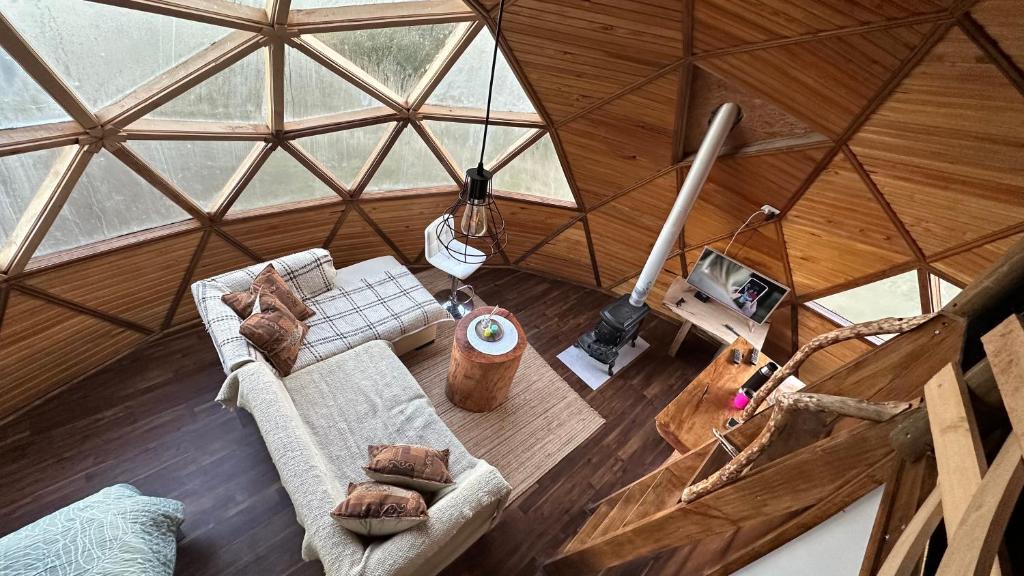 Cozy lounge inside a geodesic wooden dome with a plaid sofa, pillows, a stump coffee table, and a wood stove.