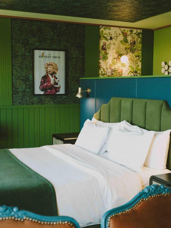Hotel room with a white bed, emerald headboard, and green walls featuring a framed Monkey Drum poster on the wall.