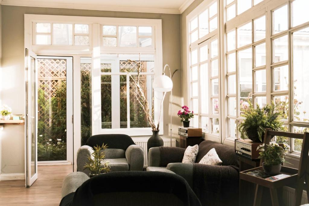 Bright living room with white-framed windows, a glass door to a garden, and dark sofas.