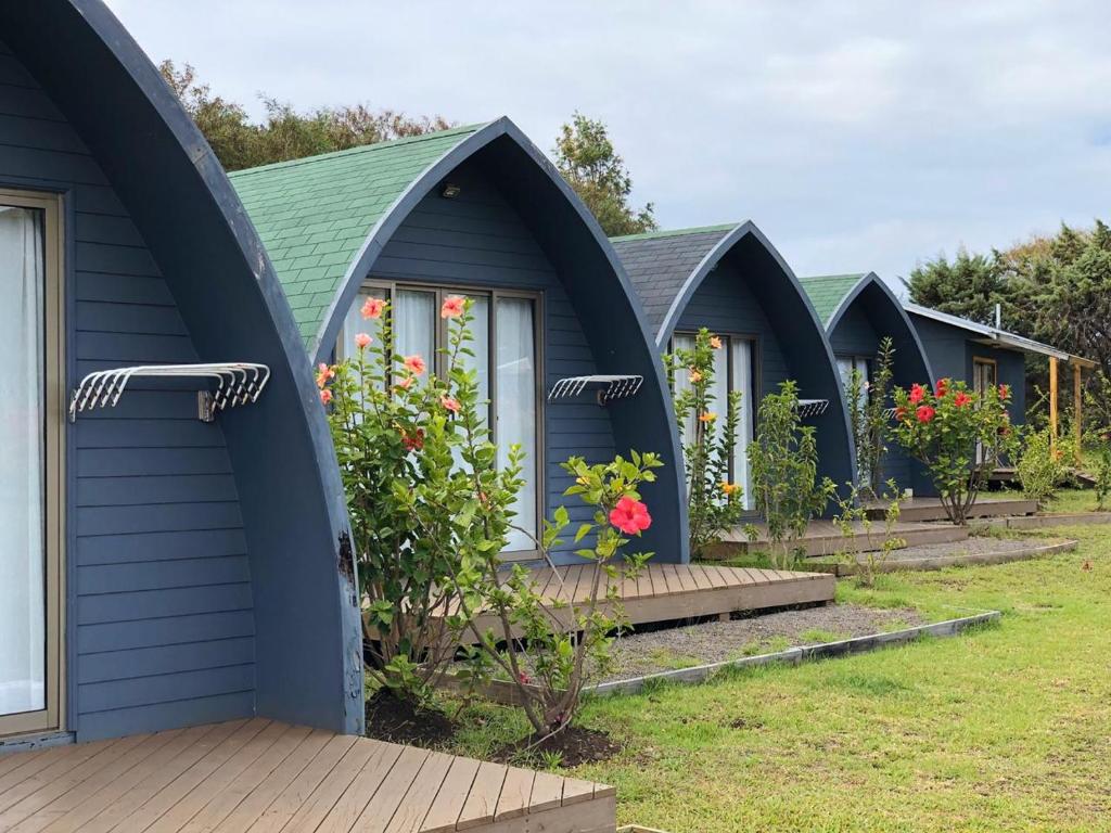 Row of blue A-frame cottages with curved roofs and small decks, lined with pink hibiscus shrubs in front