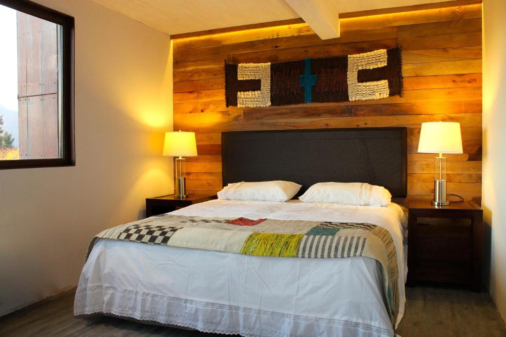 Cozy bedroom with a wooden accent wall, a large bed with white linens, and two bedside lamps on dark wood tables under warm lighting.