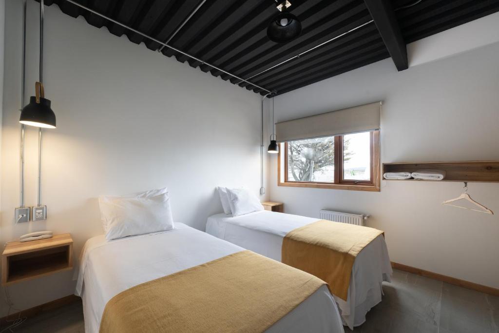 Two single beds with white linens and tan runners in a bright hotel room with a window and pendant lamps on each side.