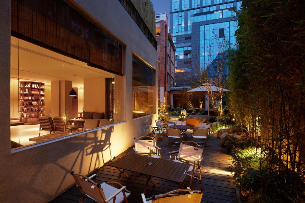 Outdoor hotel courtyard at dusk with wooden deck, white lounge chairs, and warm interior light visible through large windows.