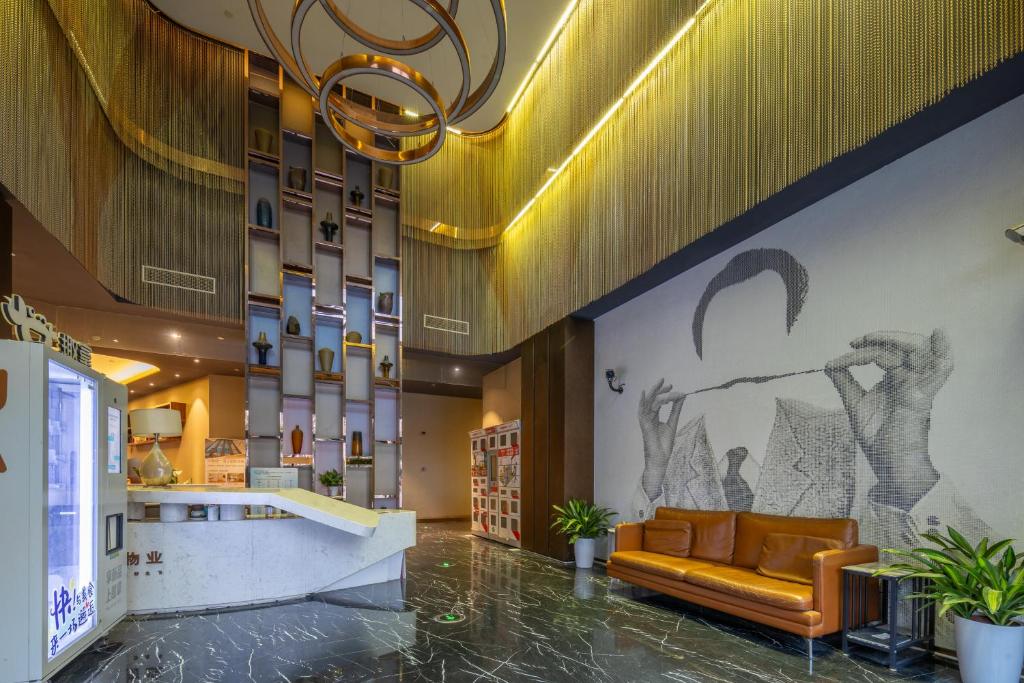 Hotel lobby with a curved white reception desk, tall shelving display, marble floor, and a brown leather sofa against a grayscale mural of a man adjusting his glasses.