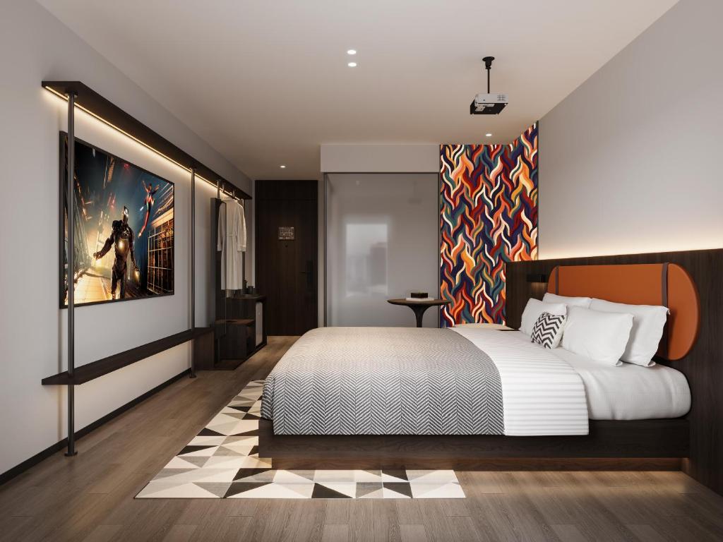 Modern hotel room with a platform bed, white bedding, and a bold orange headboard against a colorful wavy accent wall.