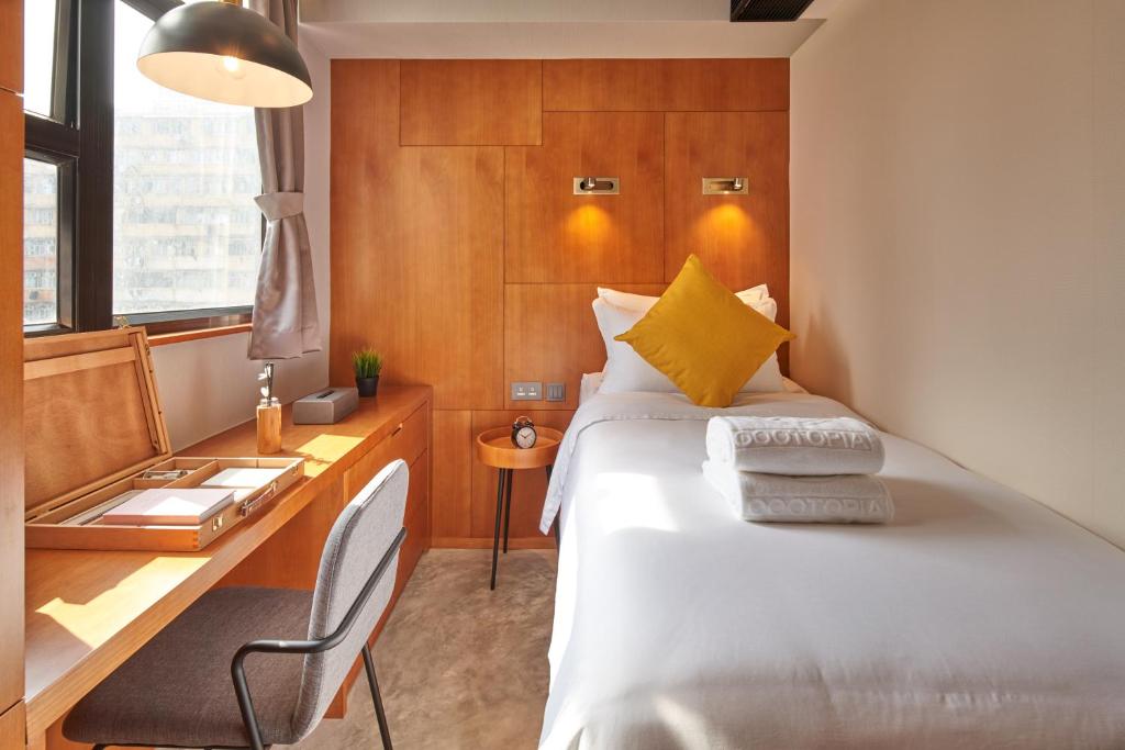 Cozy hotel room with a single bed, mustard-yellow pillow, white linens, and a wooden headboard; a desk and chair sit by the window.