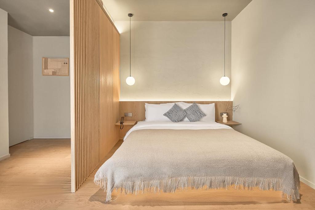 Modern hotel-style bedroom with a low wooden headboard, pendant lights, and a neutral bed setup with a beige throw.
