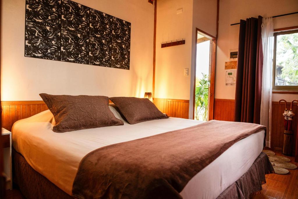 Hotel bedroom with a large bed, brown pillows and throw, warm lighting, and wooden wall paneling; doorway opens to a patio area.