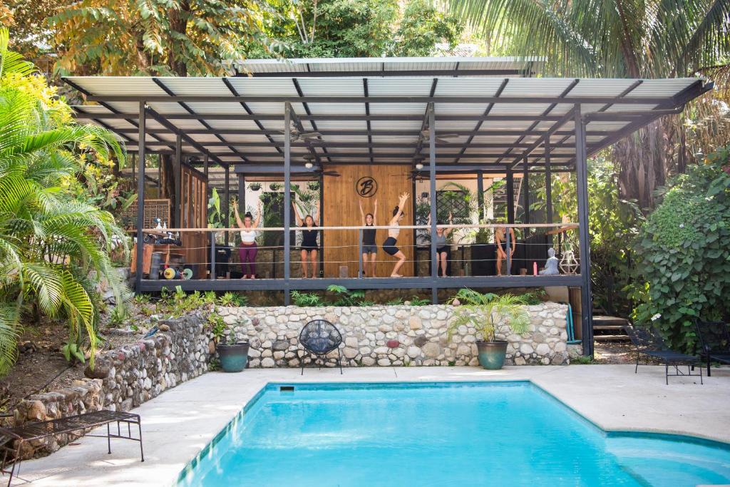 Group of people doing a workout class on a covered deck overlooking a turquoise pool in a tropical backyard.