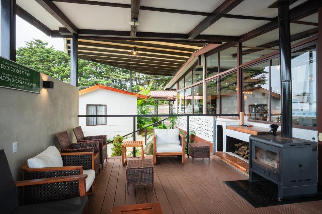 Cozy outdoor covered patio with wicker chairs, white cushions, a central coffee table, and a wood-burning stove on the right under a wooden-beam roof.