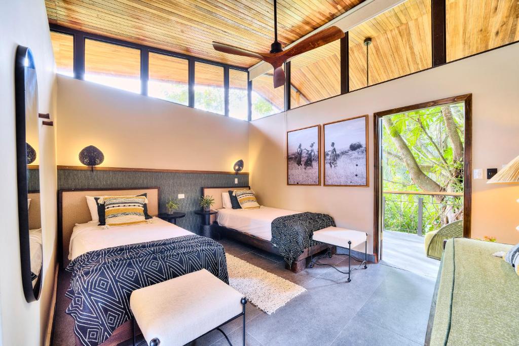 Hotel room with two twin beds and matching navy geometric bedspreads, plus a balcony door opening to greenery outside.