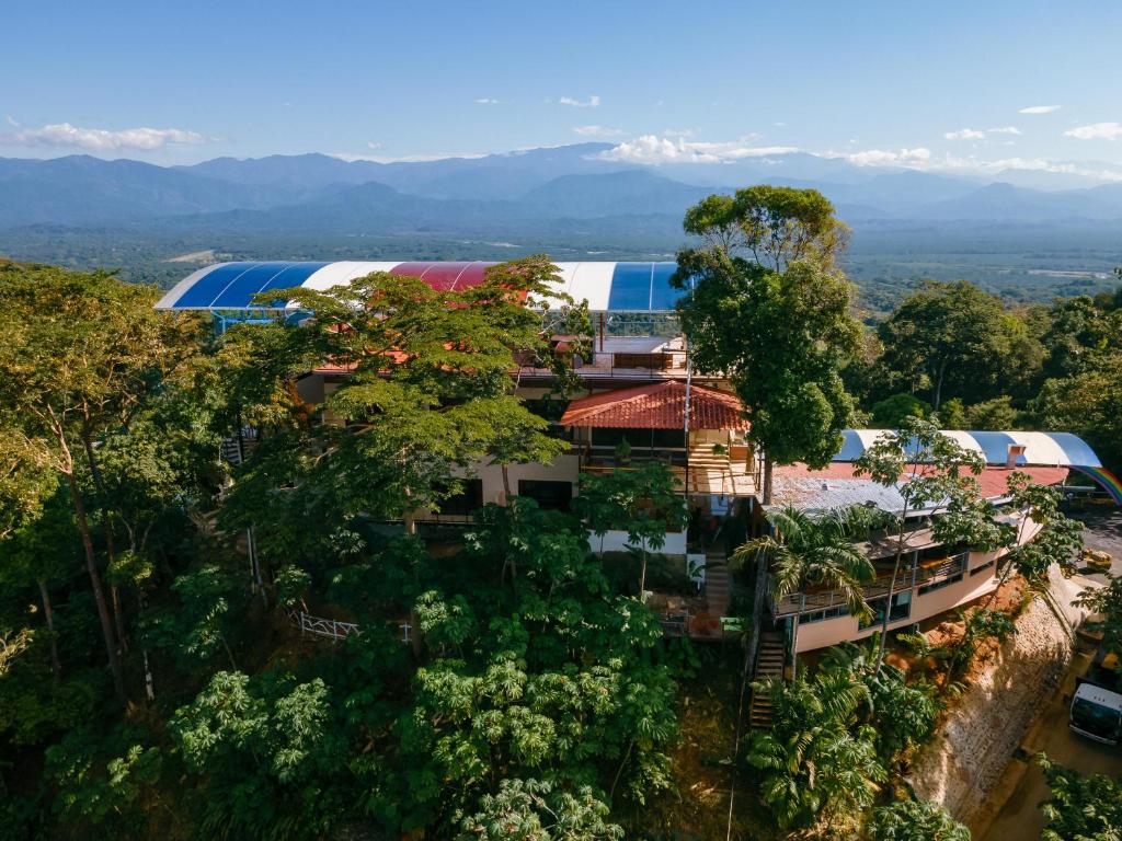 A hillside tropical resort building framed by dense trees, with a curved striped blue‑white‑red roof and distant mountains in the background.