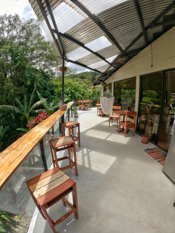 Sunny tropical outdoor patio with wooden bar stools along a glass railing, a hanging hammock chair, and sliding doors to the indoors.