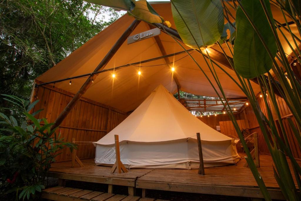 Glamping tent on a wooden deck under a canvas shelter with warm string lights in a tropical garden