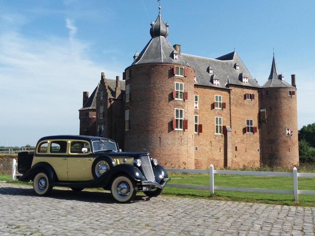 Vintage two-tone car parked on a cobblestone road with a large brick castle in the background.