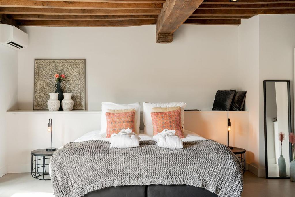Bedroom with exposed wooden beams, a large bed with white linens, orange accent pillows, and a chunky gray throw cloth.