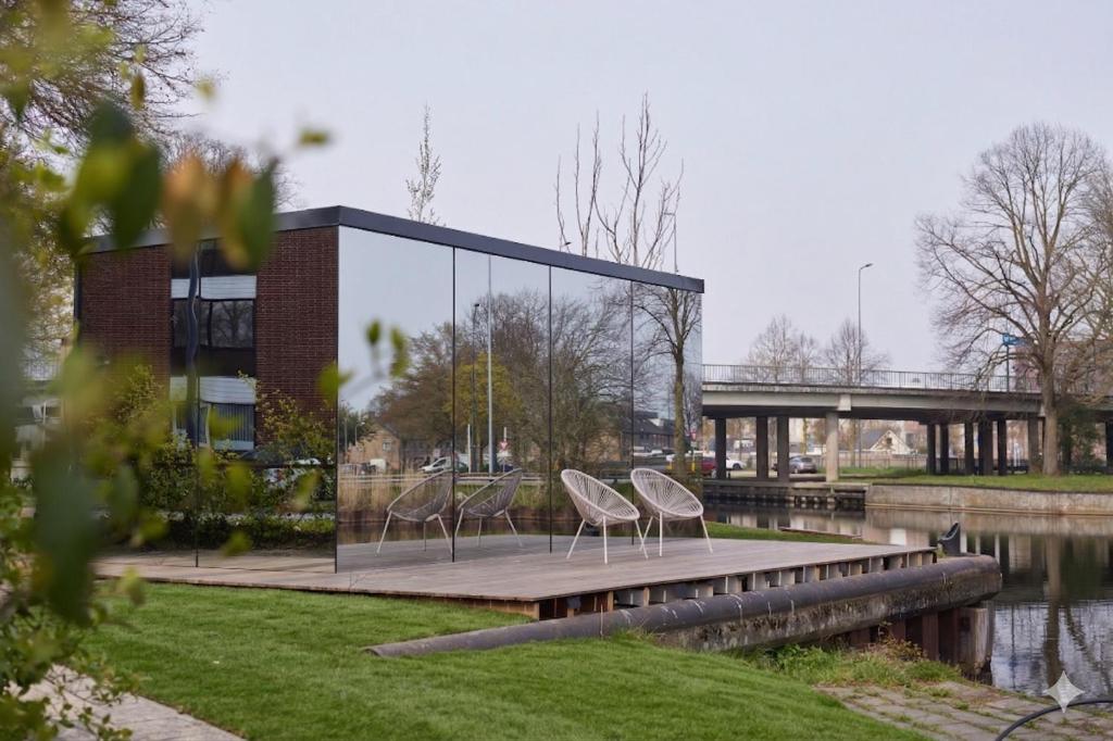 Glass-walled modern building on a wooden deck by a canal, with two white chairs facing the water.