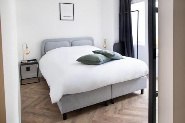 Modern gray upholstered bed with white bedding and two green pillows in a bright bedroom.