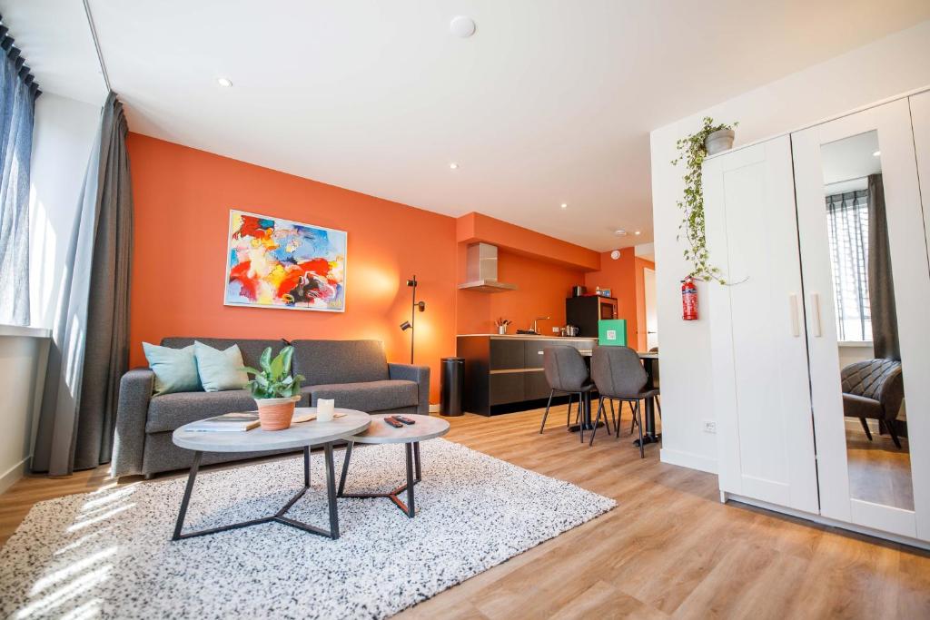 Open-plan living space with orange accent wall, gray sofa, abstract art, and round coffee tables on a rug.
