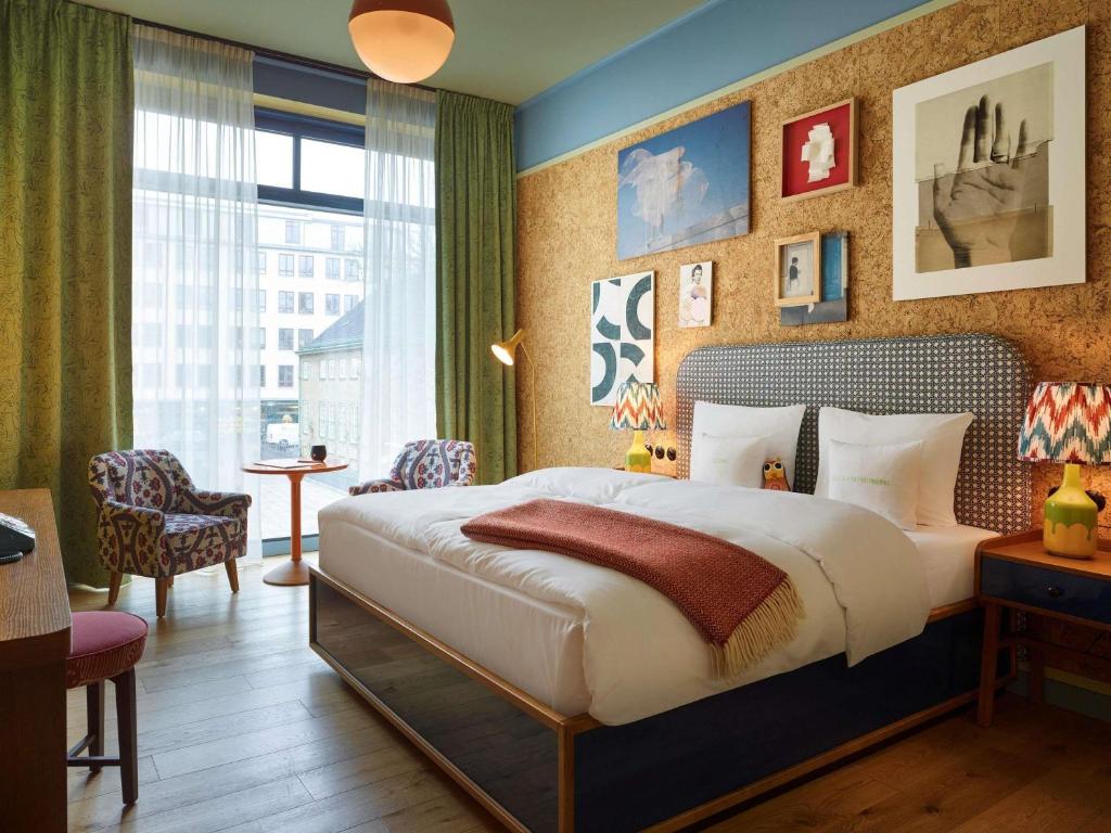 Bright hotel bedroom with a large window, a cork accent wall, and a neatly made queen bed with white linens.