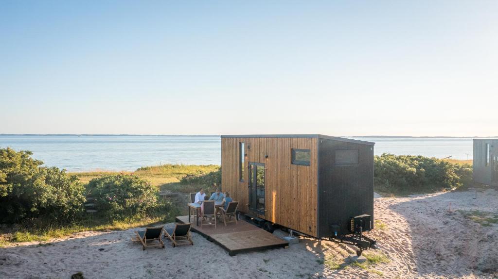 Wooden beach cabin on sand with a group dining at an outdoor table, overlooking the sea.