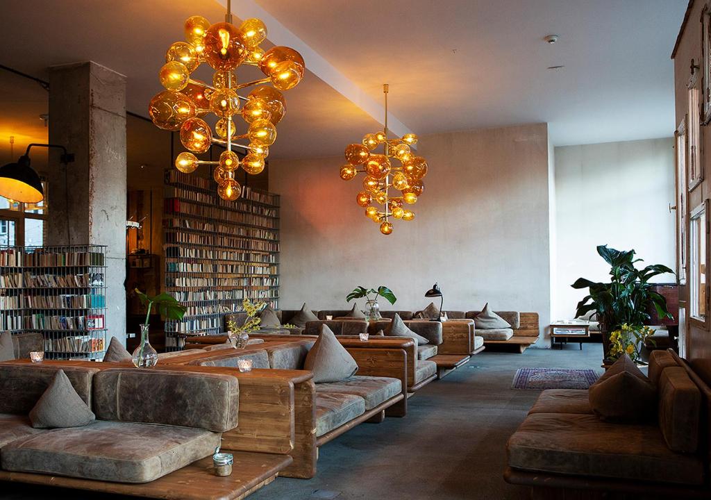 Cozy modern lounge with low wooden sofas, gray cushions, glass vases, and gold spherical chandeliers above.