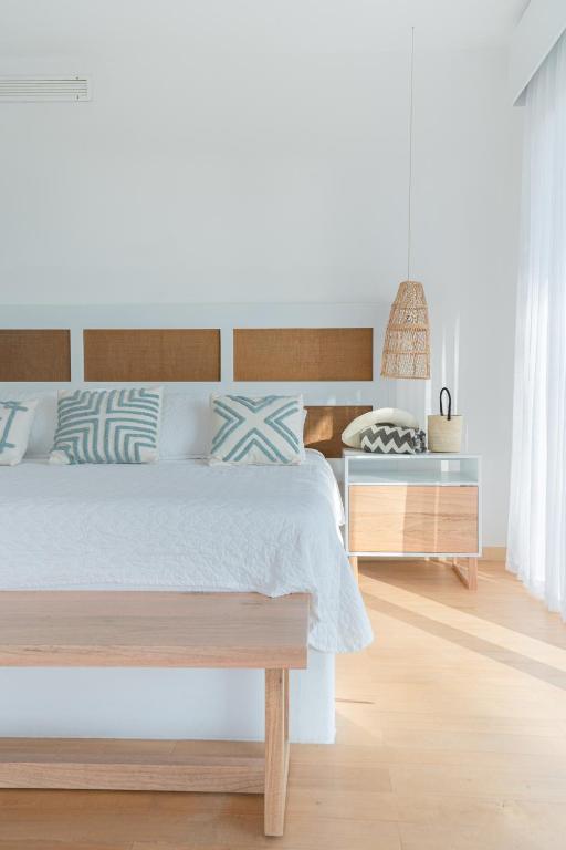 Bright minimalist bedroom with white walls, light wood bed, and teal patterned pillows.
