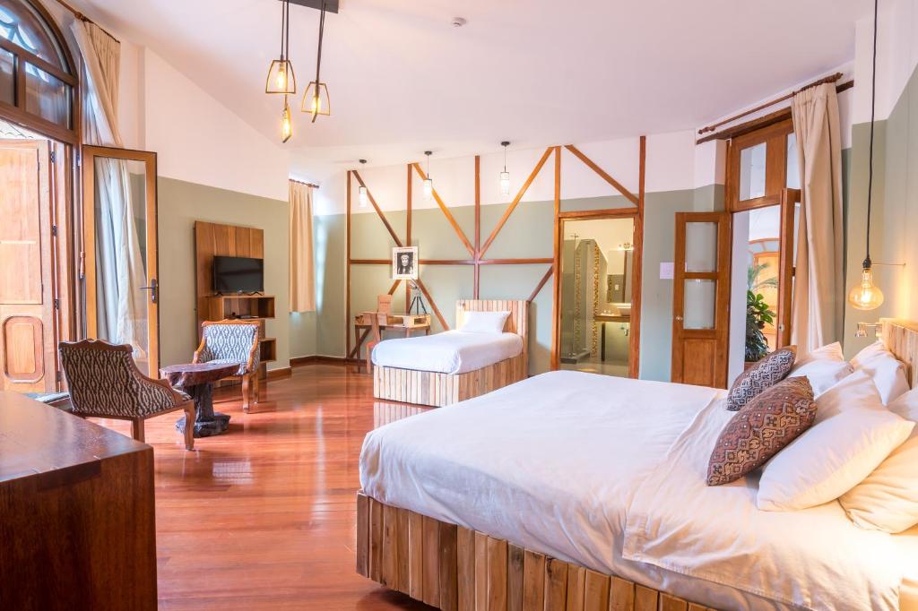 Spacious hotel room with two large, white-blanket beds, wooden accents, and warm lighting; seating area and balcony door to the left.