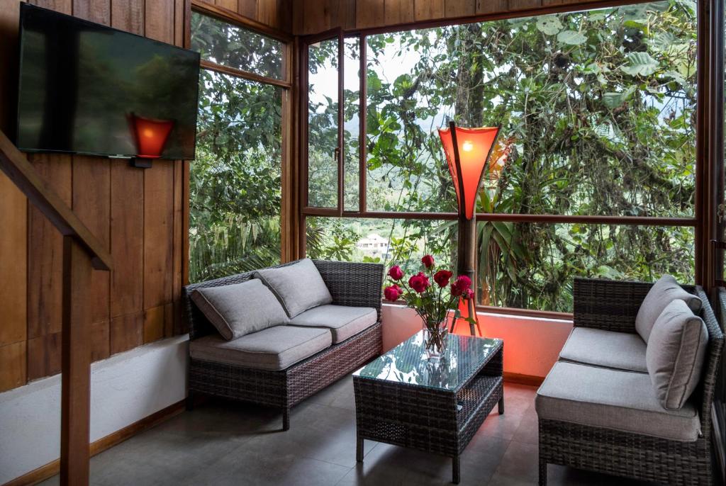 Cozy wicker sofa set with gray cushions around a glass coffee table in a sunlit screened porch, red flowers in vase and greenery outside.