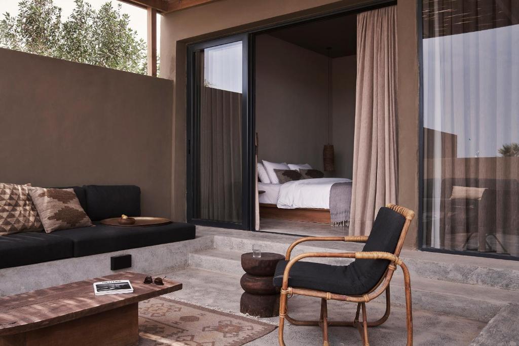 Outdoor patio area with a dark sofa, woven chair, and low wooden coffee table, opening to a bedroom via a sliding glass door with beige curtains.