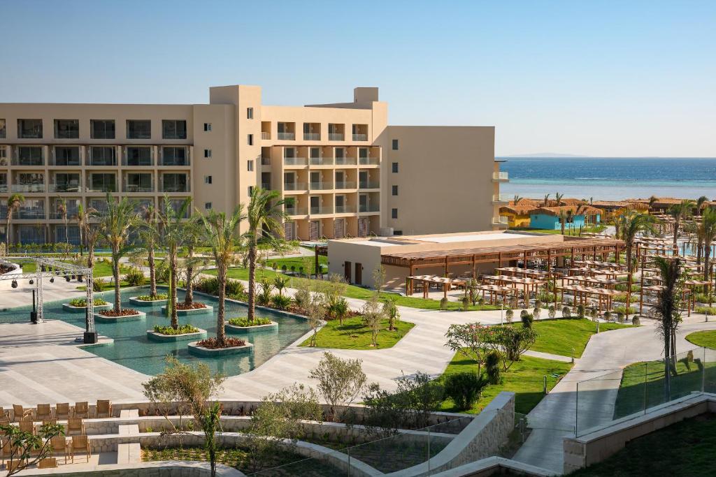 Resort hotel with a multi-story building, pool with palm trees, and a beachside lounge area facing the ocean.
