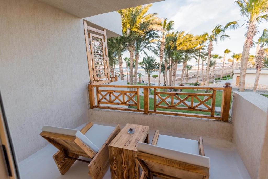 Wooden balcony with two chairs and a small table, overlooking palm trees and a beach/ocean view.