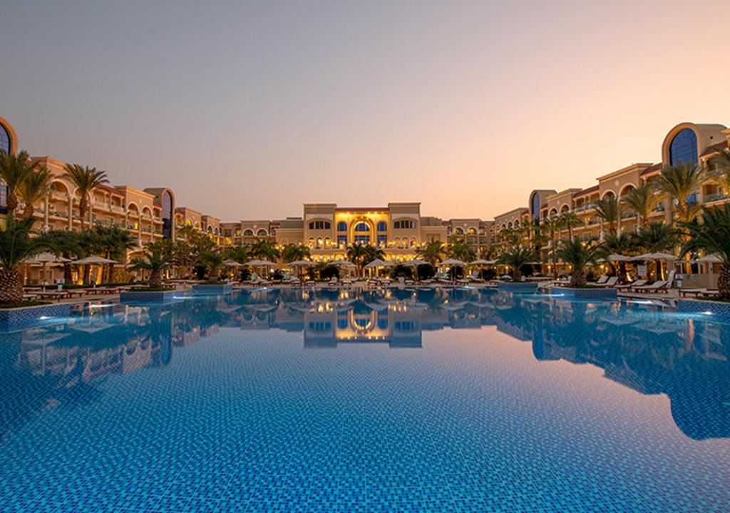 Resort pool at sunset with palm trees and a grand hotel facade reflected in the water