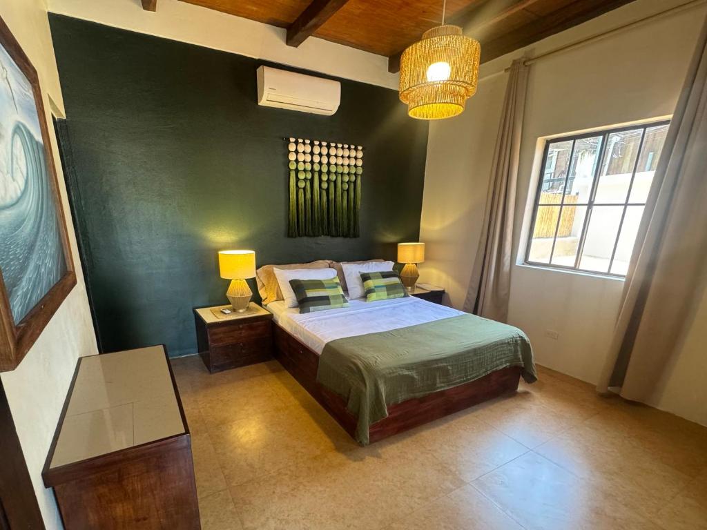 Bedroom with a green feature wall, queen bed, two bedside tables with lamps, a dresser, and a wicker ceiling light.