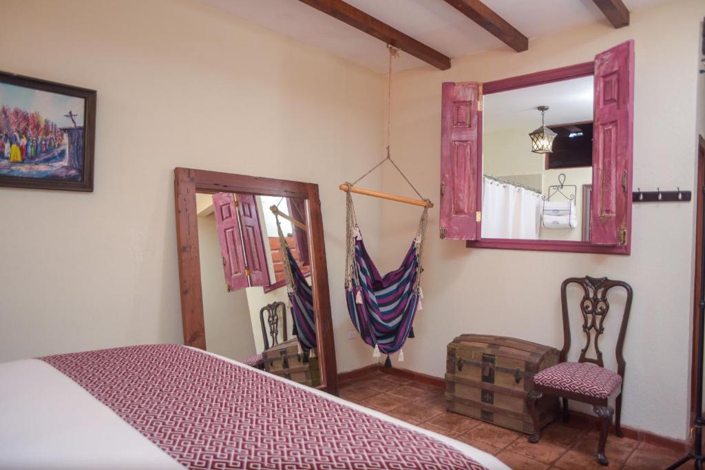 Cozy bedroom with a striped hammock chair, a wooden-framed mirror, and a pink window shuttered wall with a wooden chest nearby.