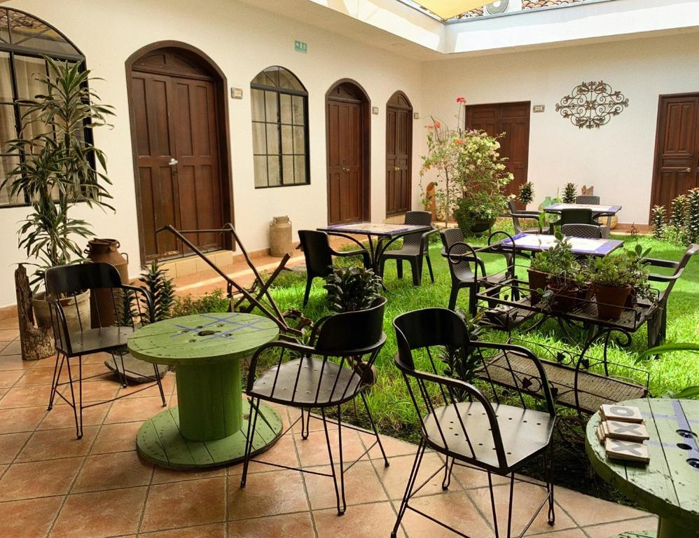 Courtyard seating with green tables, black metal chairs, and potted plants on a tiled floor, enclosed by white walls and wooden doors.