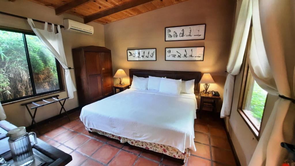 King-bed hotel-style bedroom with white linens, two nightstands, lamps, and a wooden wardrobe.