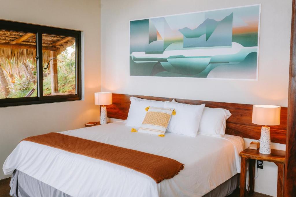 Bright hotel bedroom with a white bed, orange throw, wooden headboard, abstract wall art, and bedside lamps.