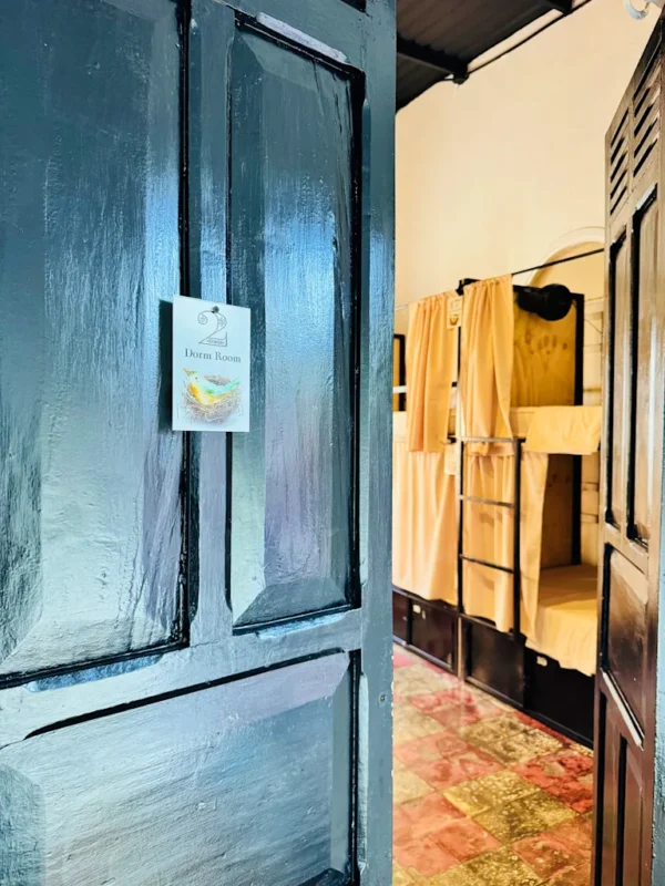 Blue dormitory door open to a room with yellow bunk beds and beige curtains; a small sign on the door reads 'Dorm Room'.