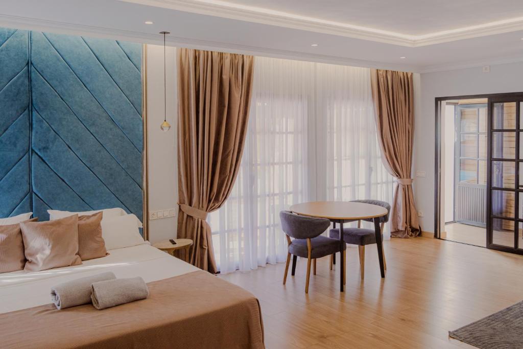 Hotel room featuring a teal upholstered headboard, neatly made bed with beige pillows and towels, and a round table with two chairs by large windows with curtains.
