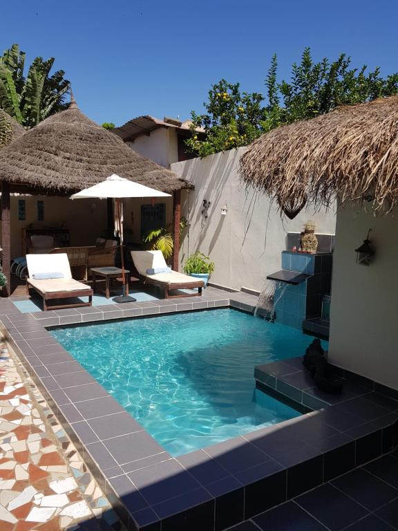 Outdoor pool area with blue tile edging, lounge chairs, and thatched-roof huts in a sunny courtyard.