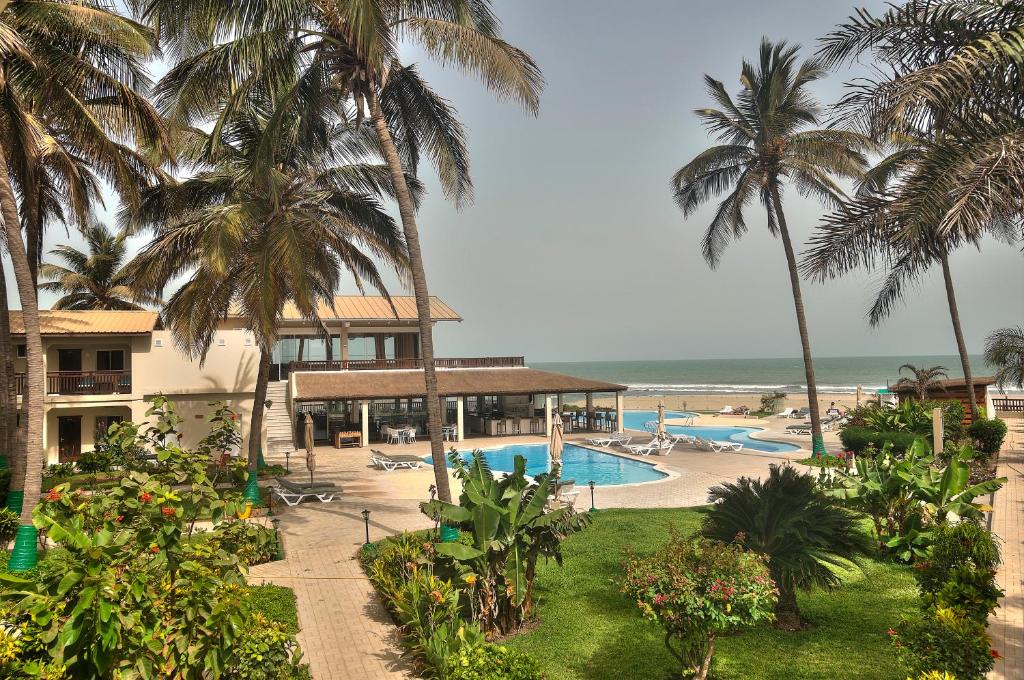 Resort pool area with lounge chairs, palm trees, and a beach in the background.