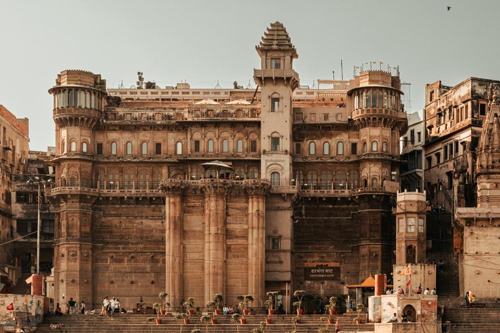 Facade of a historic Indian palace with a tall central tower, rounded corner pavilions, and steps with visitors