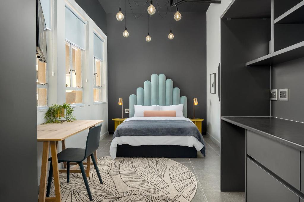 Hotel room with a queen bed and a sky-blue upholstered curved headboard, two yellow nightstands, and hanging bulbs.