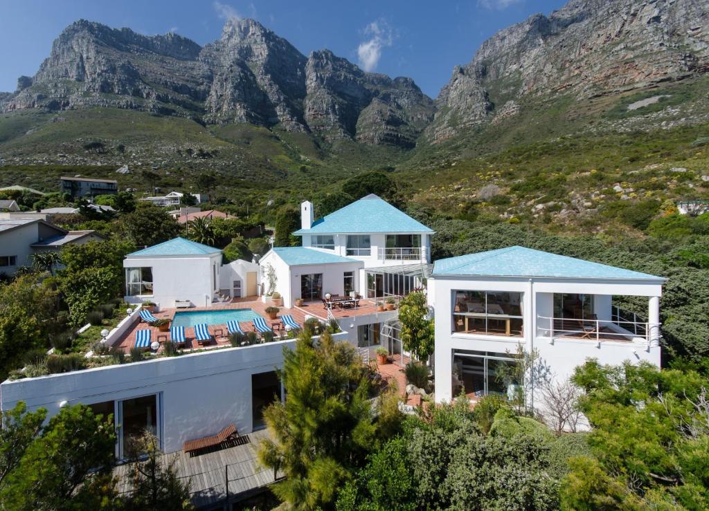 White villa complex with turquoise roofs and a pool deck, set on a hillside against rugged mountains and greenery.